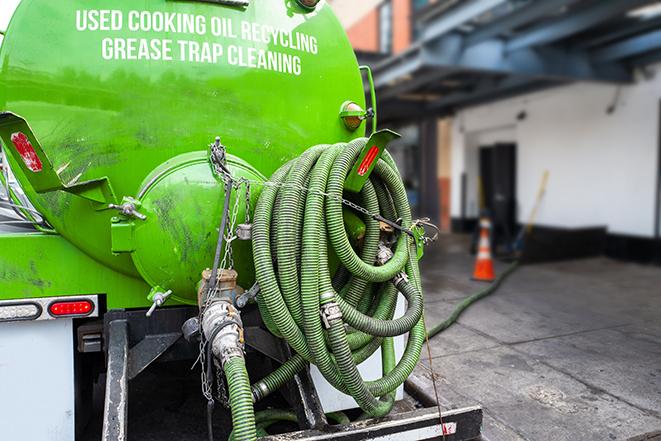 a professional plumber using a pump to empty a grease trap in Alexander NY